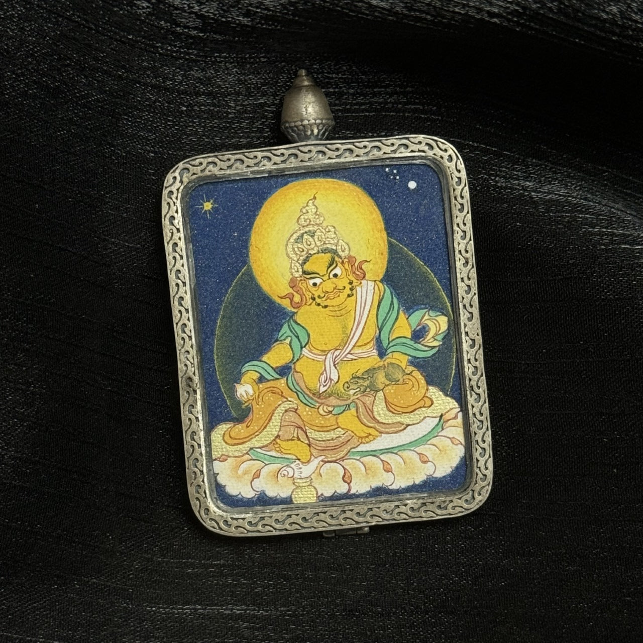 Detailed front view of Yellow Jambhala Tibetan thangka pendant featuring wealth deity iconography, coarse mineral pigment application, and silver frame craftsmanship