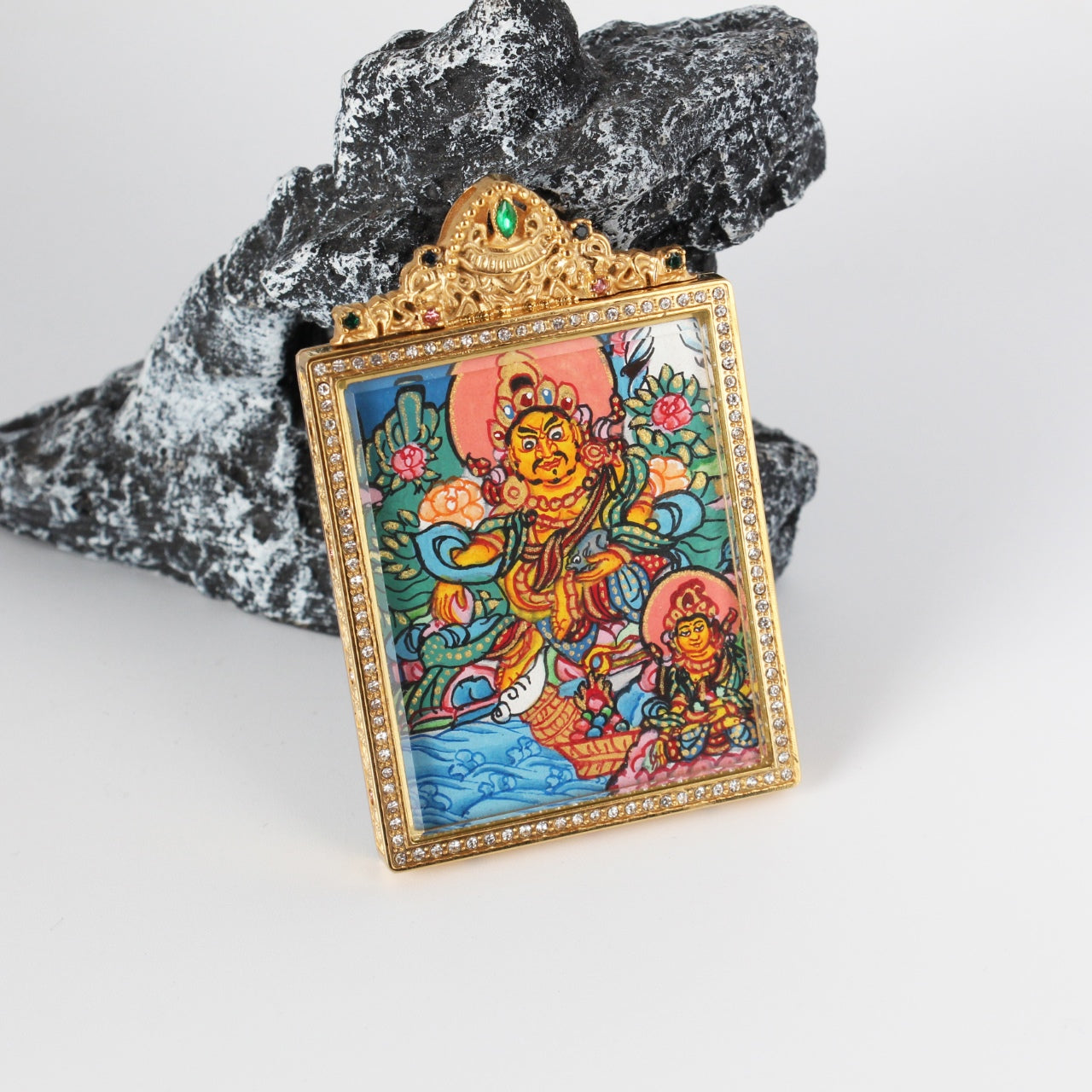 Angled view of dual deity Yellow Jambhala and Vasudhara mini thangka pendant with vivid hand-painted mineral pigment details and gold-tone jeweled titanium steel frame