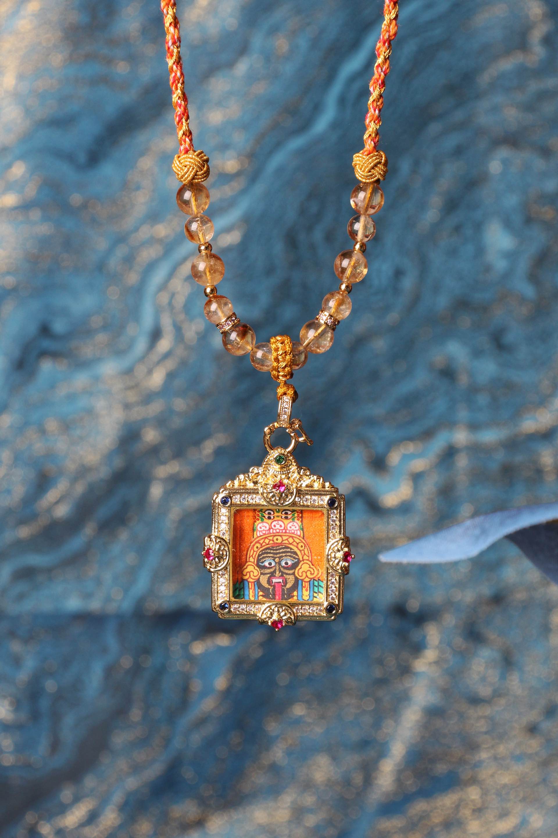 Hanging lifestyle photo of a Zaki Lham hand-painted mini thangka pendant in a gemstone square frame on a beaded necklace