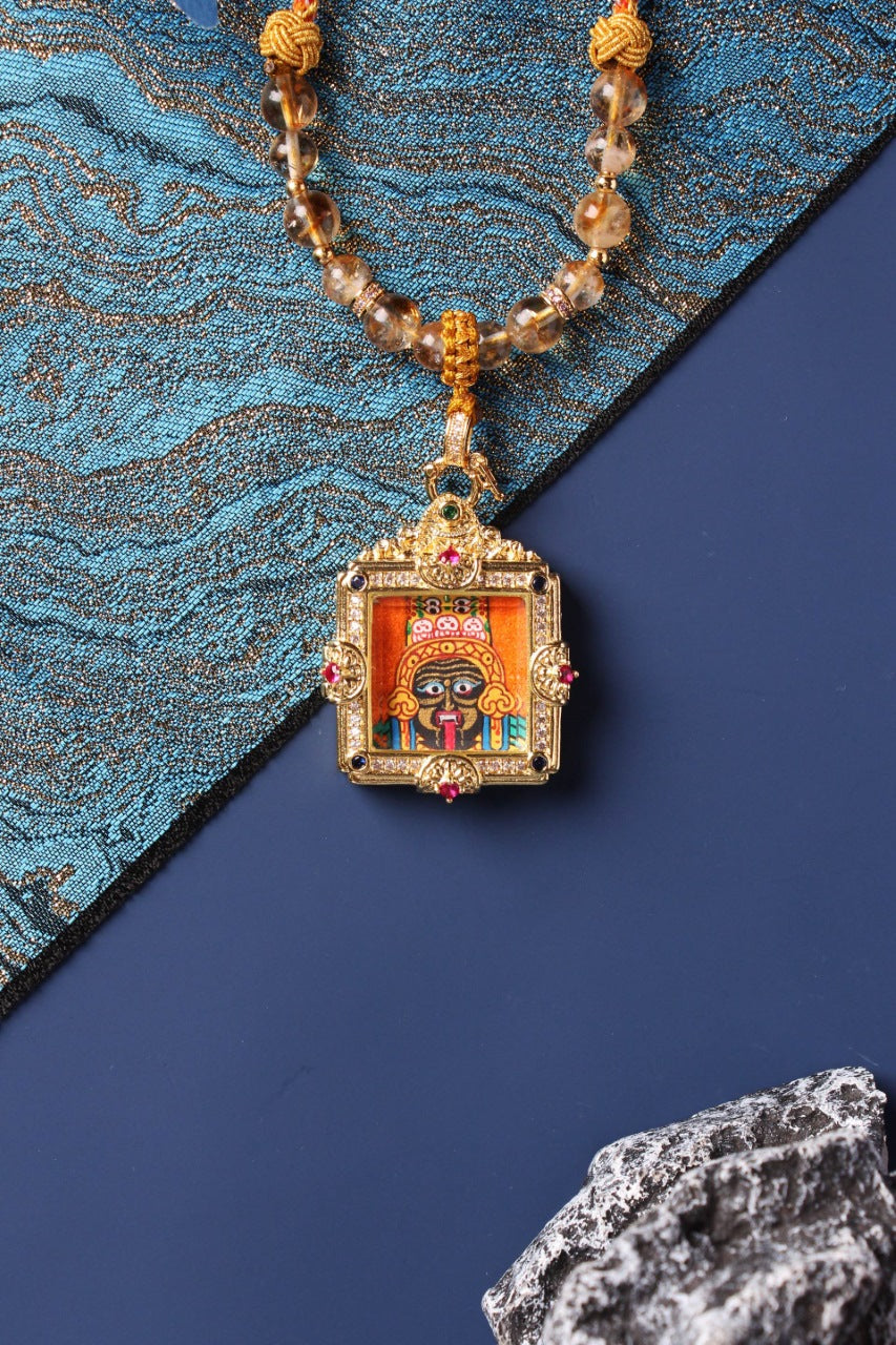 Close-up of a Zaki Lham hand-painted mini thangka pendant in an ornate square frame with gemstone accents on a beaded necklace