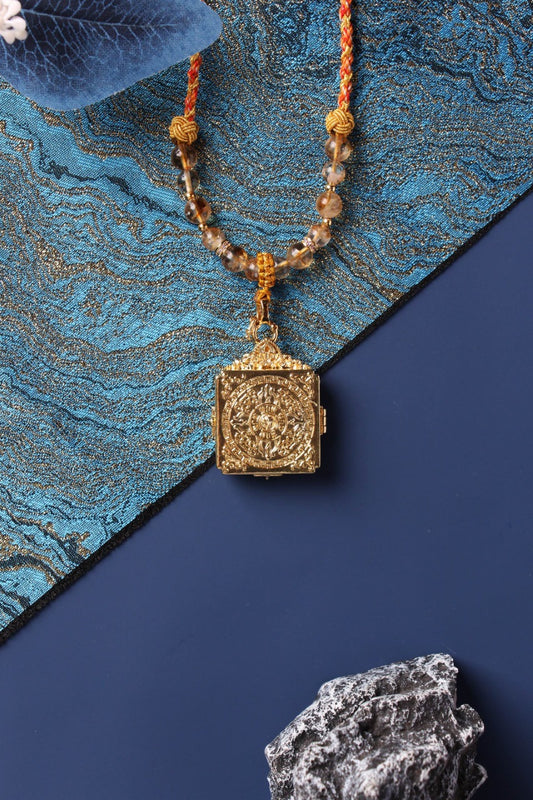Back view of the Zaki Lham mini thangka pendant showing an ornate relief-patterned case on a beaded necklace