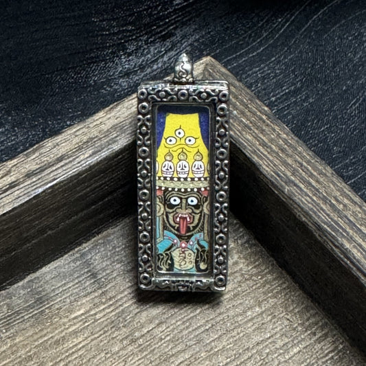 Front view of Zaki Lhamo Tibetan wealth deity amulet pendant in a metal case, Rebgong hand-painted with natural mineral pigments, displayed on a wooden tray.