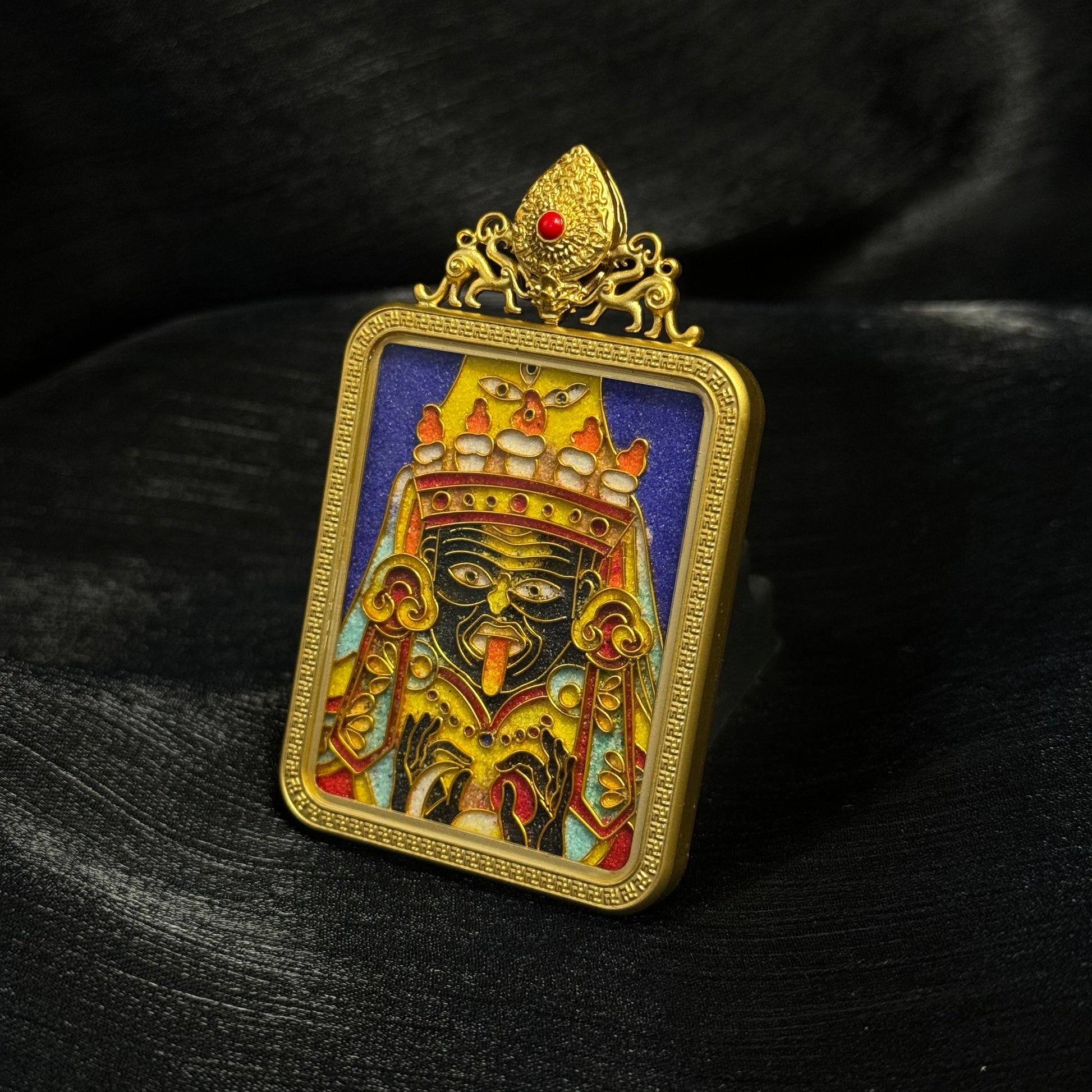 Detailed view of Zaki Lhamo cloisonné enamel pendant showing deity facial features, colorful enamel background, and ornamental gold frame design.