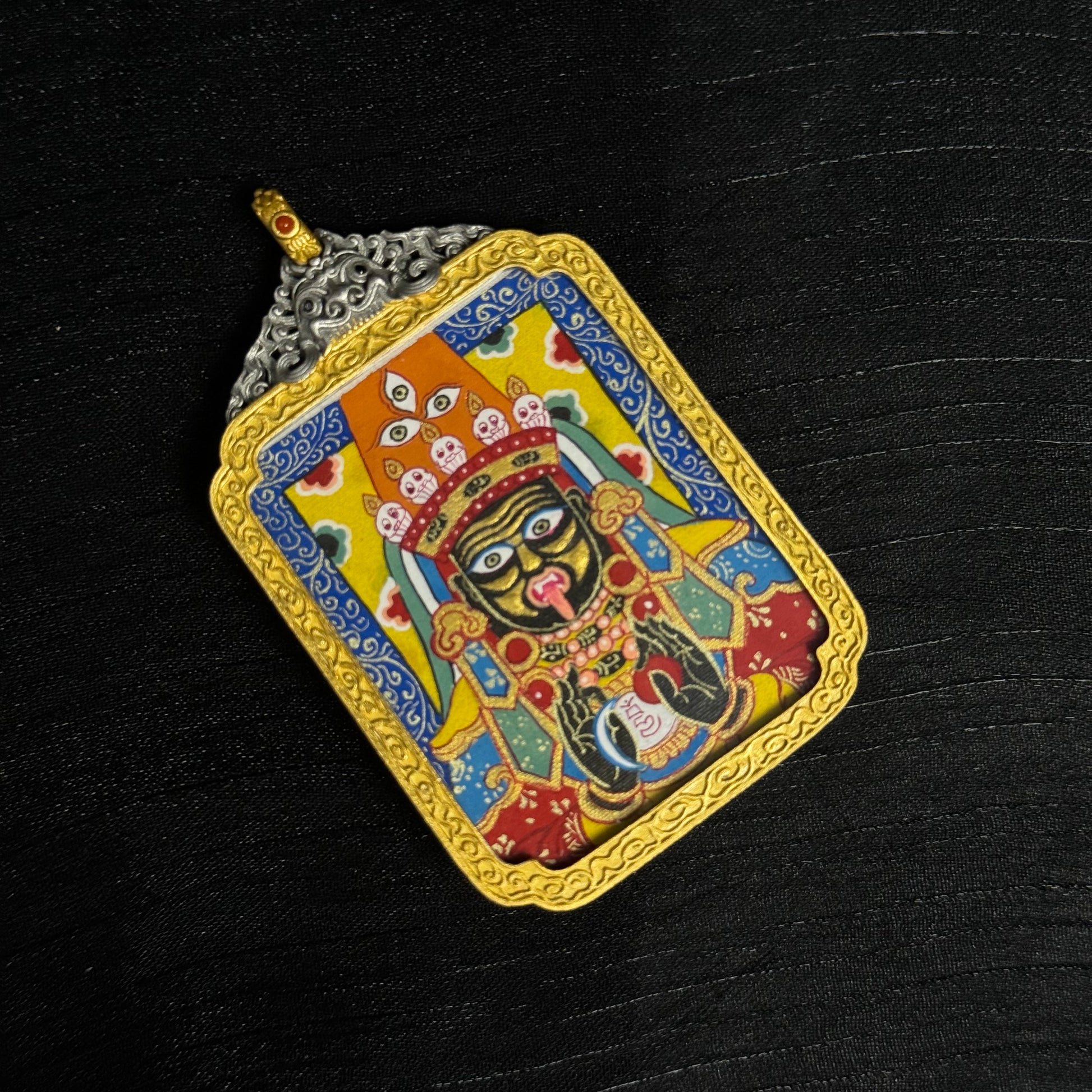 Close-up view of Zaki Lhamo miniature thangka pendant displaying hand-painted mineral pigment details, vibrant colors, and ornate gold frame.