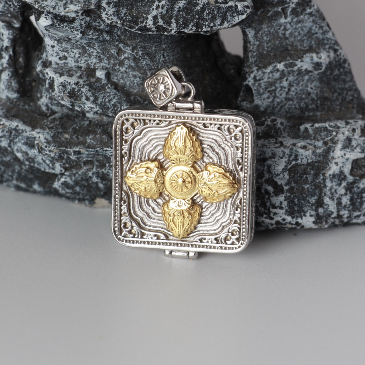 Back view of Zaki Lhamo mini thangka pendant showing gold vajra cross relief on square silver-plated case with decorative borders.