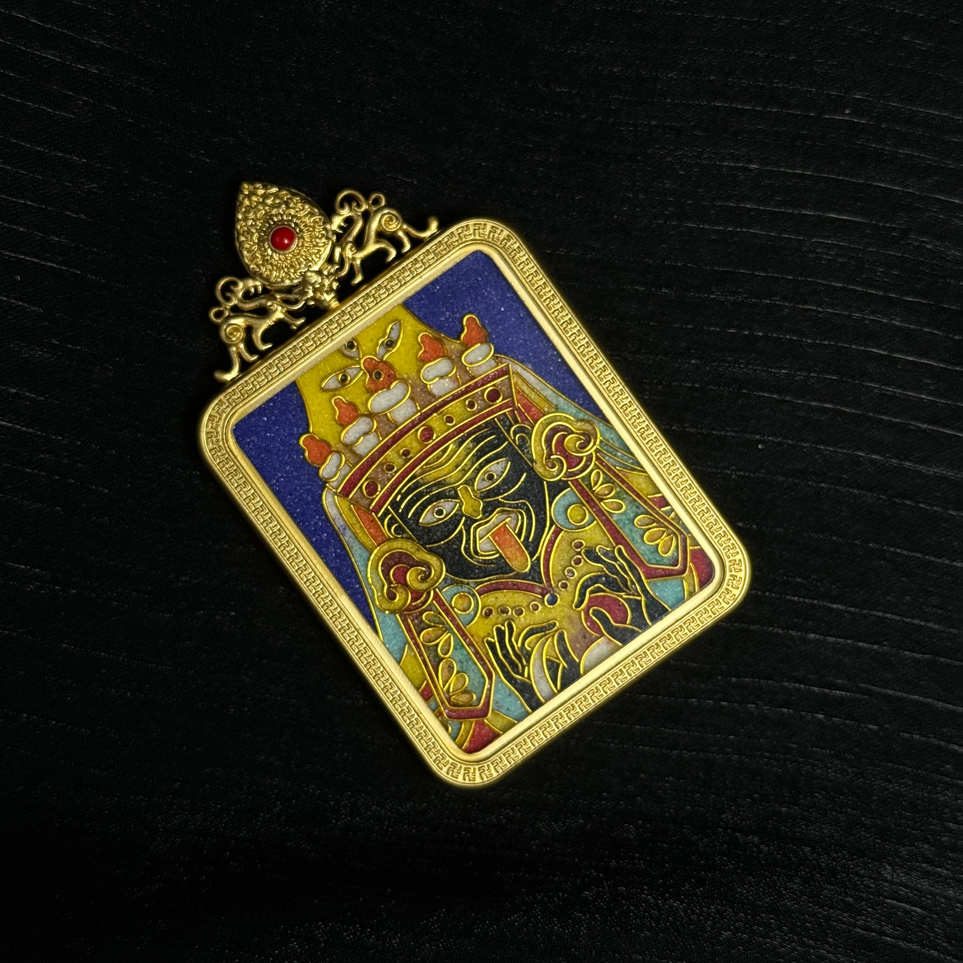 Close angled view of Zaki Lhamo mini thangka pendant revealing detailed cloisonné wire patterns, vibrant enamel colors, and gold plated copper frame.