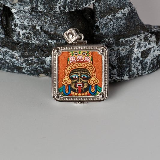 Front close-up of Zaki Lhamo mini thangka pendant with hand-painted mineral pigments, orange background, and detailed facial features in a square silver-plated frame.