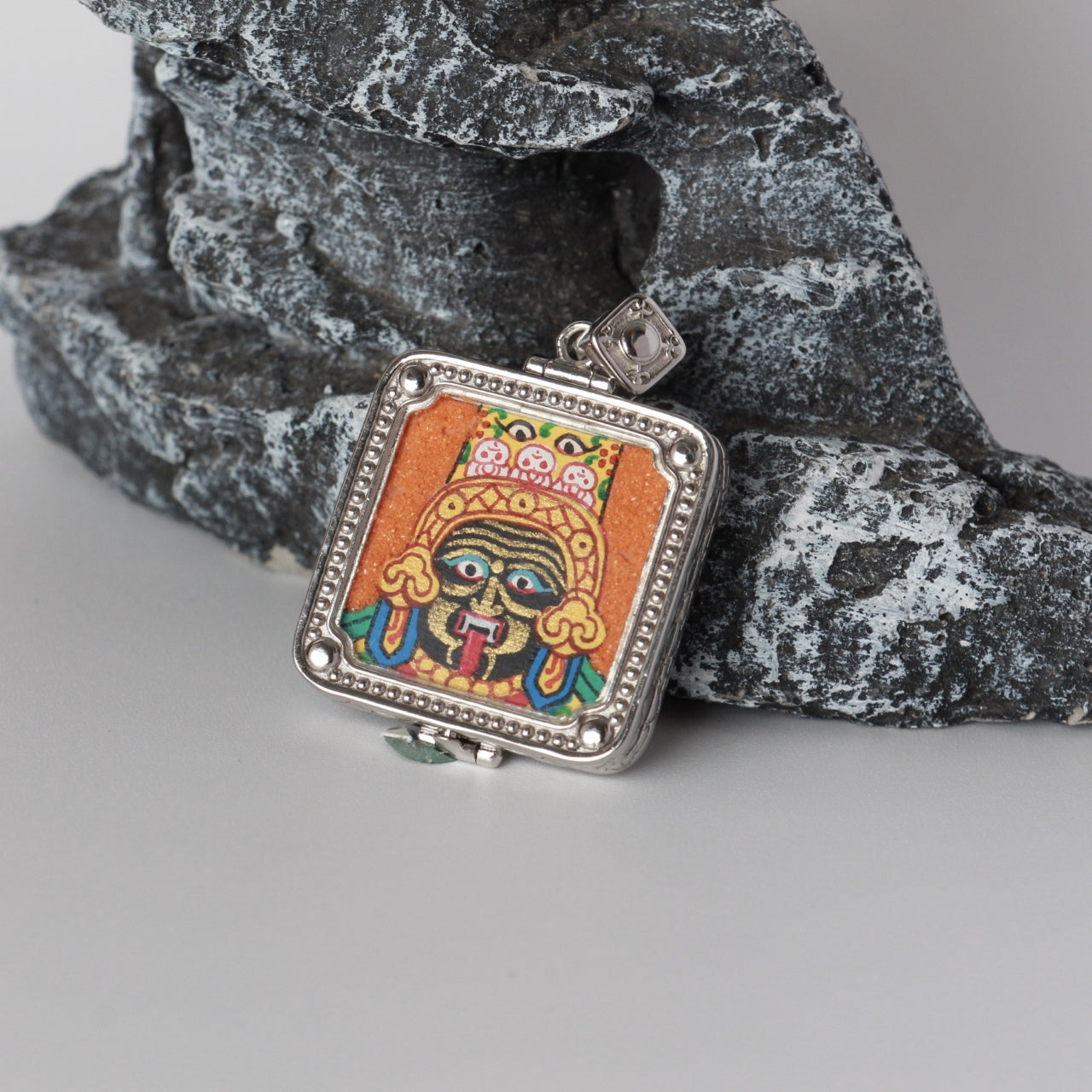 Centered front view of Zaki Lhamo mini thangka pendant showing the hand-painted image set in a square silver-plated case with patterned border.