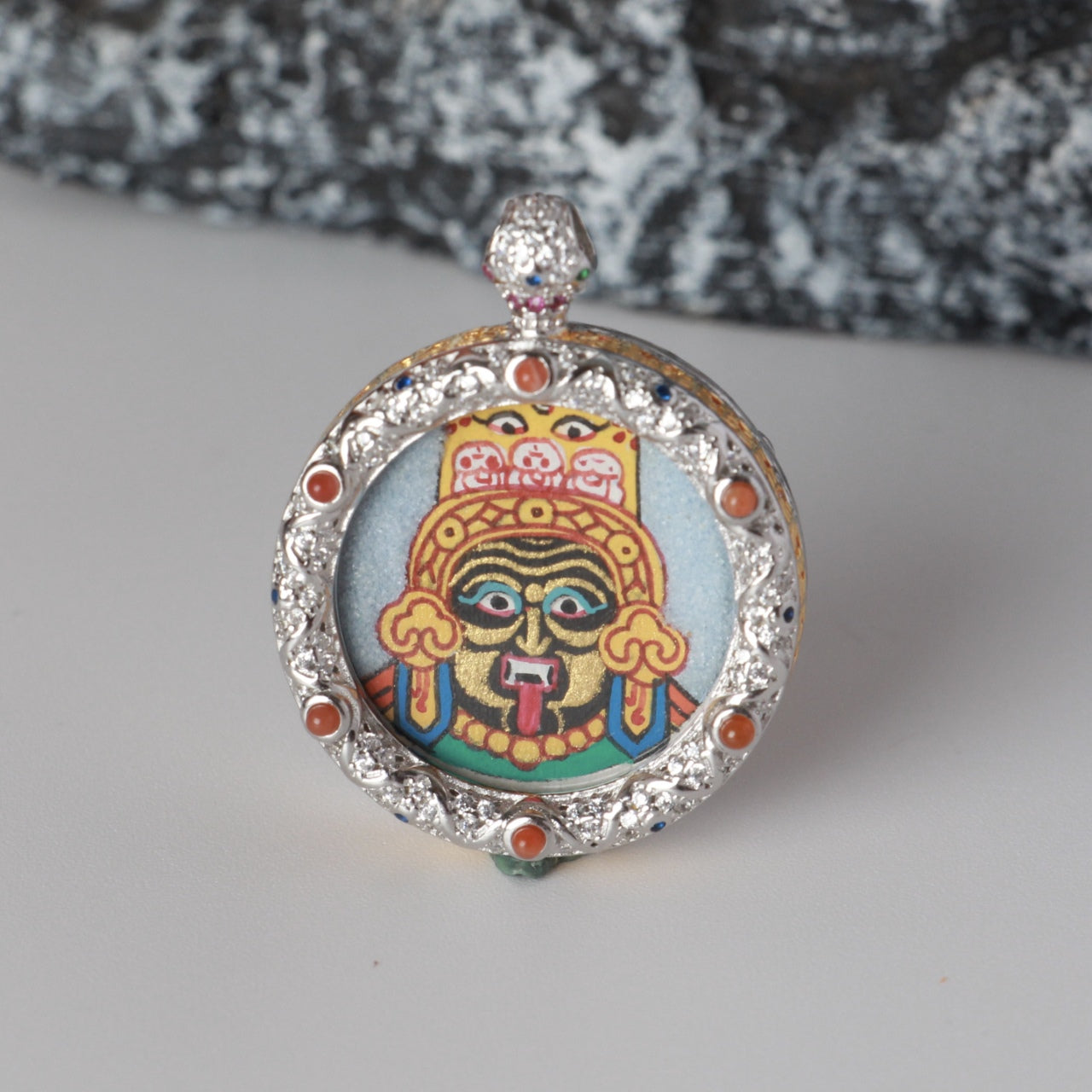 Front view of a Zaki Lhamo mini thangka pendant, hand-painted with coarse mineral pigments, set in a round jewelry-grade copper case with ornamental detailing.