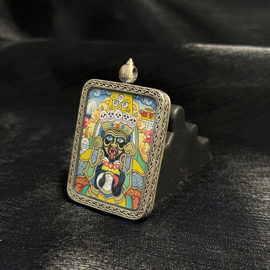 Angled view of Zaki Lhamo mini thangka pendant showing the detailed hand-painted Tibetan deity portrait, mineral pigment colors, and ornamental silver frame with traditional carving.