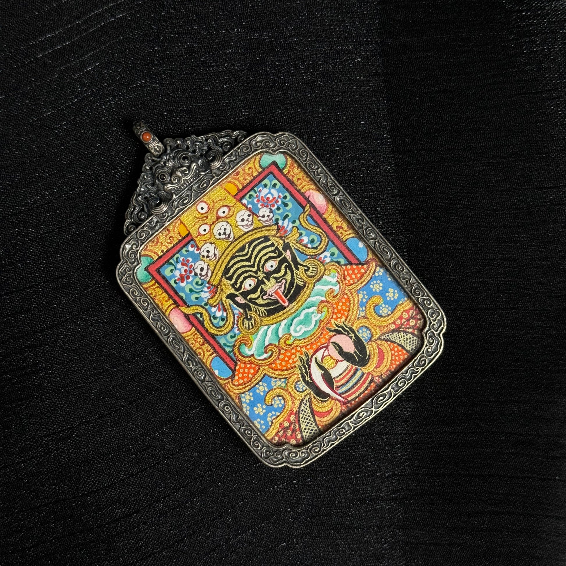 Top angled view of Zaki Lhamo mini thangka pendant displaying the ornate silver frame, pendant loop, and vibrant mineral pigment thangka painting.