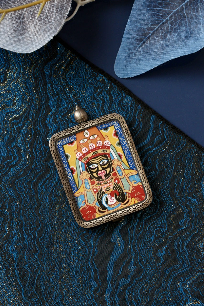 Zaki Lhamo hand-painted mini thangka pendant in a rectangular 925 silver case, photographed on blue brocade fabric