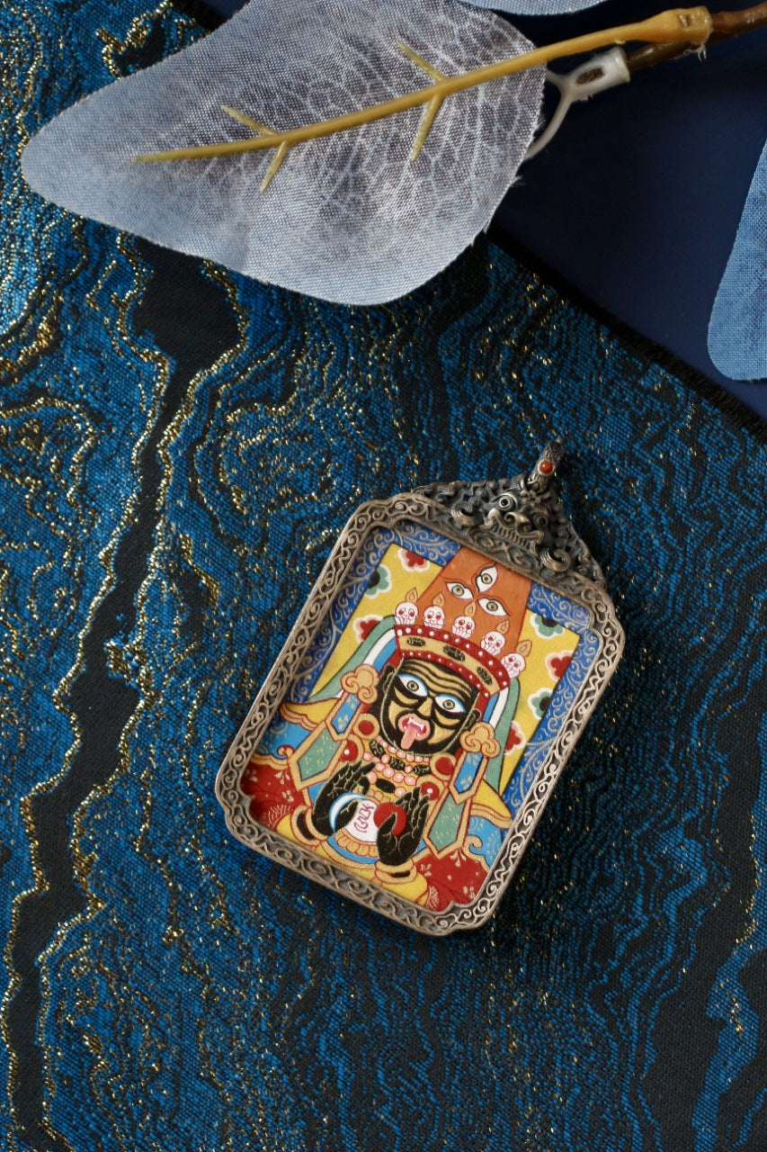 Zaki Lhamo hand-painted mini thangka pendant in an ornate gawu-style 925 silver case with decorative top, on blue brocade fabric