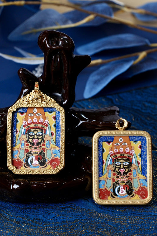 Zaki Lhamo mini thangka pendants displayed upright on a stand, showing blue-background hand-painted image and gold-tone copper cases in two frame styles.