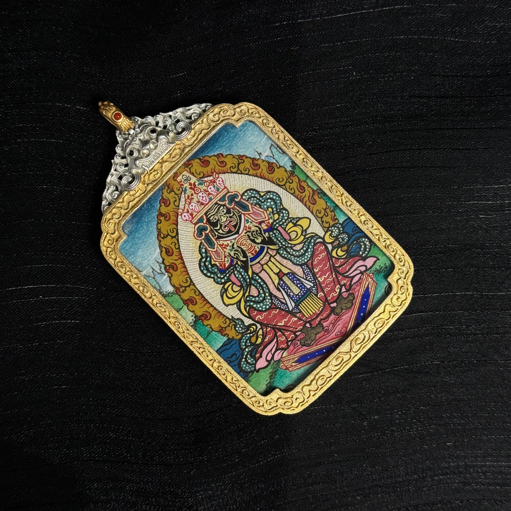 Close-up view of Zaki Lhamo miniature thangka pendant displaying hand-painted mineral pigments, vibrant colors, and intricate decorative frame.