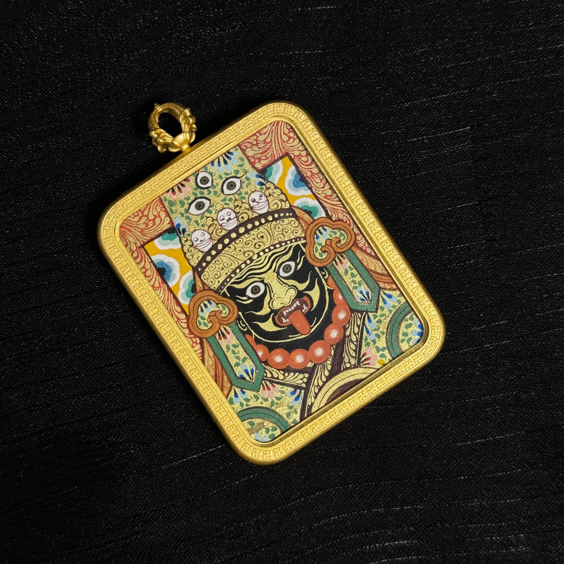 Top-down angled view of Zaki Lhamo mini thangka pendant showing the decorative gold frame, pendant loop, and finely painted Tibetan thangka artwork using natural mineral pigments.