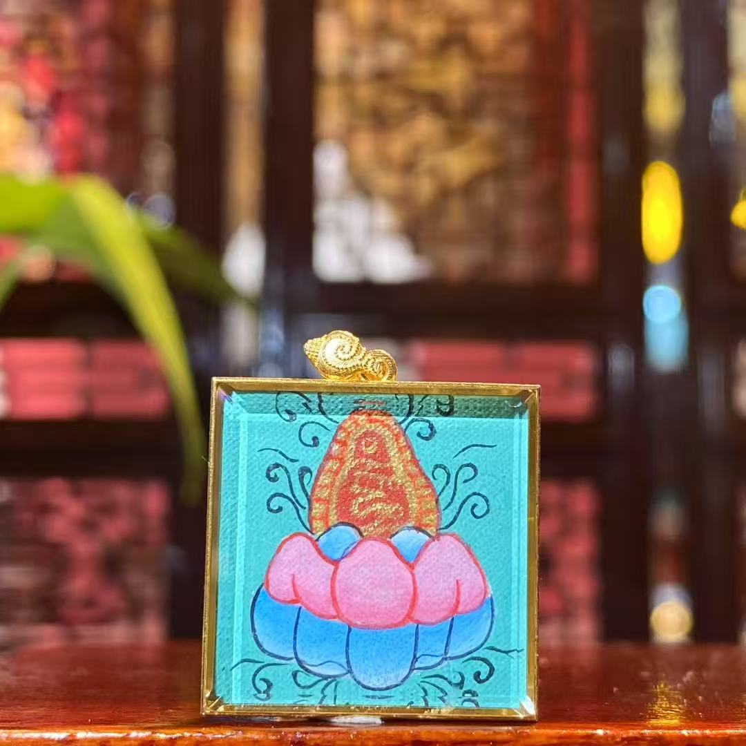 Back view of the Zaki Lhamo thangka pendant featuring the mantra seed syllable engraved inside an 18K gold gau box with double-sided sapphire crystal protection