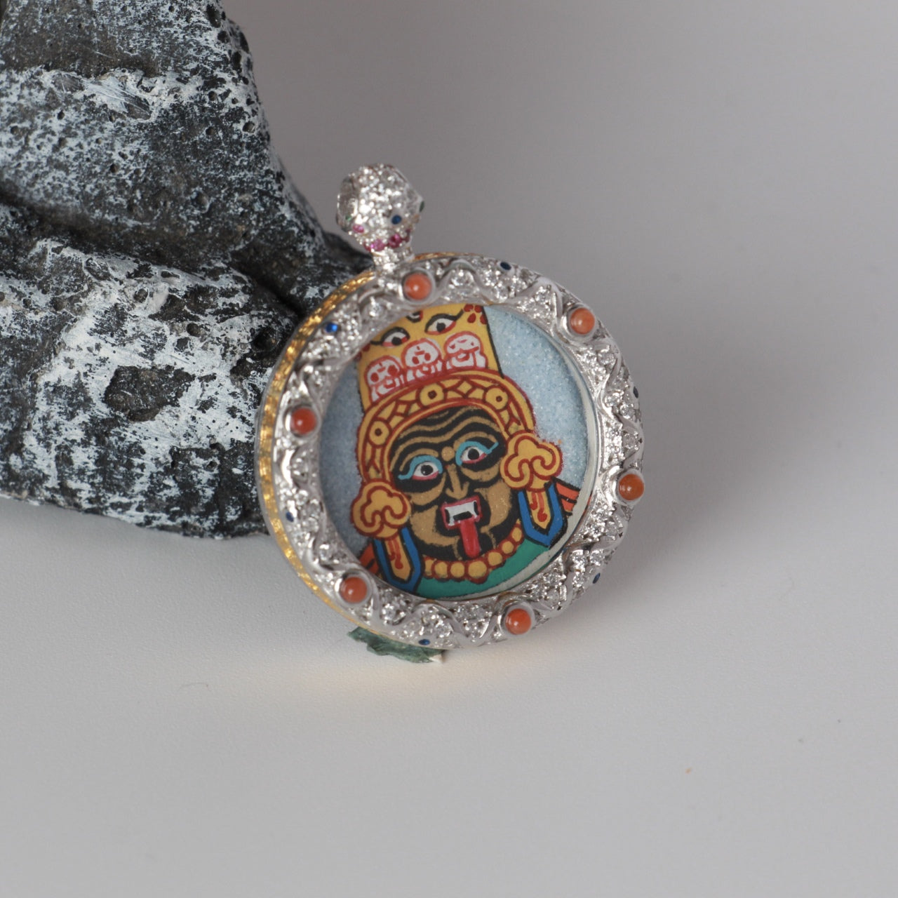 Close-up view of the Zaki Lhamo thangka pendant focusing on facial features, symbolic elements, and the coarse mineral pigment texture.