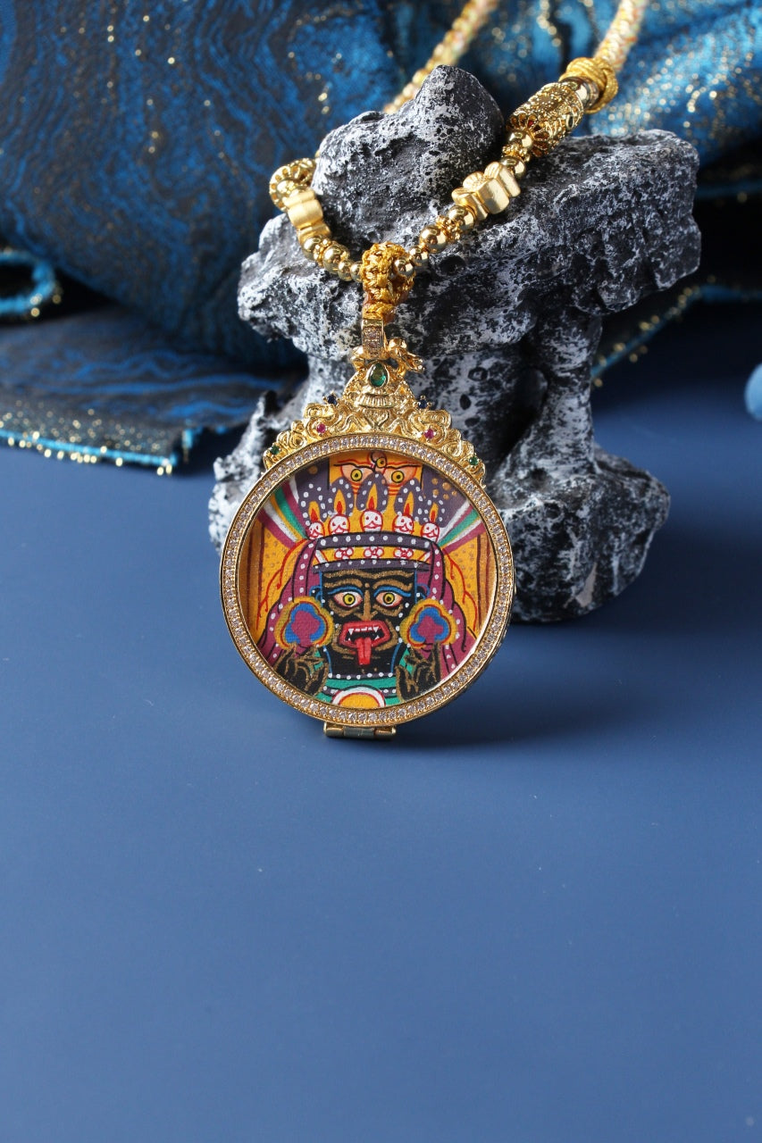 Zaki Lhamo mini thangka pendant displayed with gold-tone beaded necklace, round frame design, detailed facial iconography and mineral pigment painting