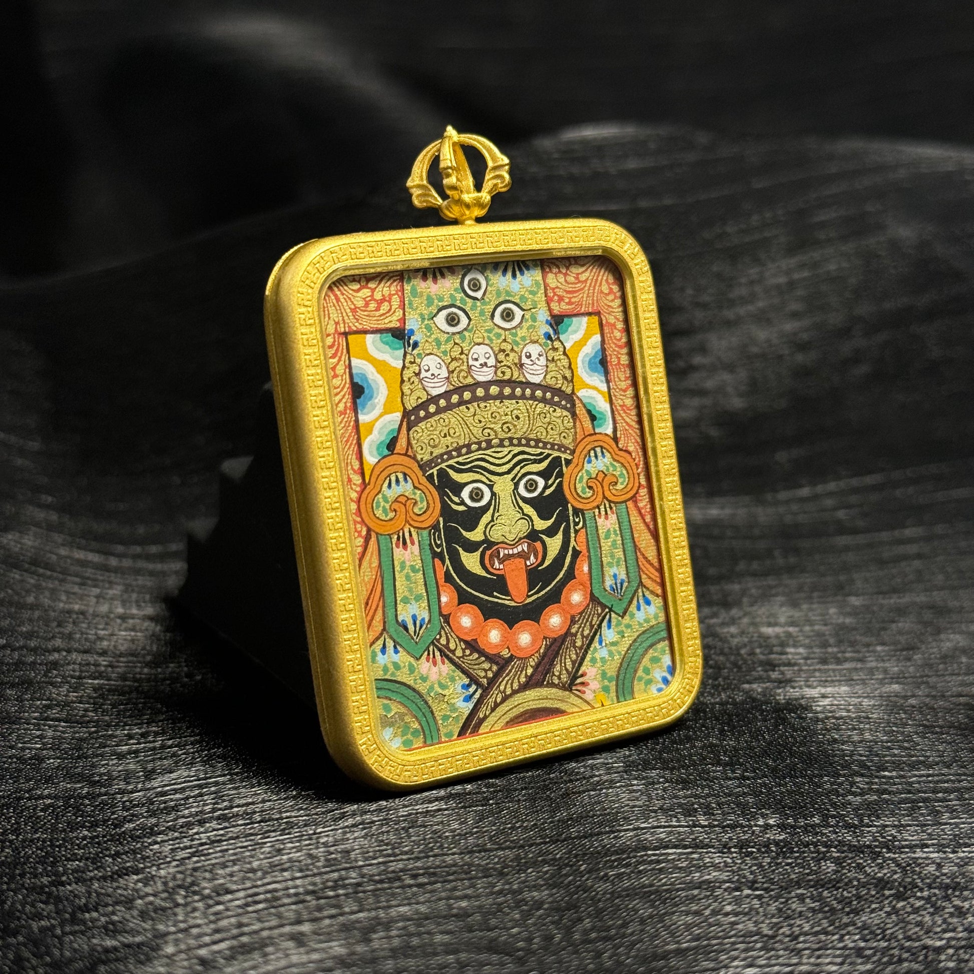 Angled view of Zaki Lhamo Tibetan mini thangka pendant showing detailed mineral pigment painting, flowing linework, and traditional Rebgong thangka craftsmanship inside a gold pendant frame.