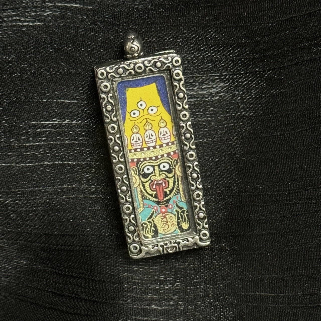 Close-up front view of Zaki Lhamo Tibetan wealth deity amulet pendant, Rebgong hand-painted mineral pigment artwork inside a metal case.