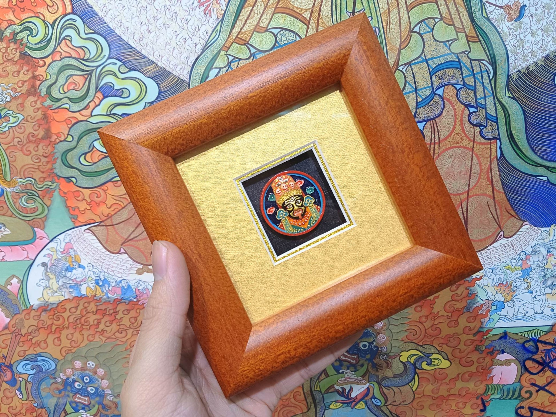 Angled hand-held view of Zaki Ram framed tsa-tsa thangka artwork highlighting Indonesian cypress frame and colorful mineral pigment painting