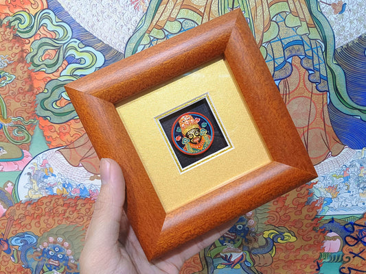 Angled hand-held view of Zaki Ram framed tsa-tsa thangka artwork highlighting Indonesian cypress frame and colorful mineral pigment painting