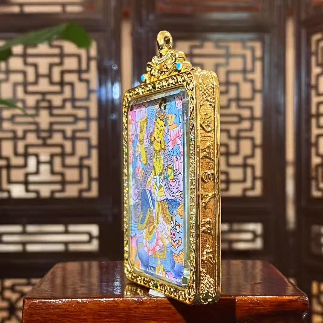 Gold-plated copper Ghau pendant with handcrafted details, framing a traditional Tibetan thangka