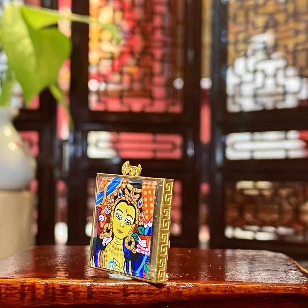 Side view of a double-sided Manjushri Bodhisattva mini thangka pendant showing the 18K gold Gau box and sapphire crystal protection