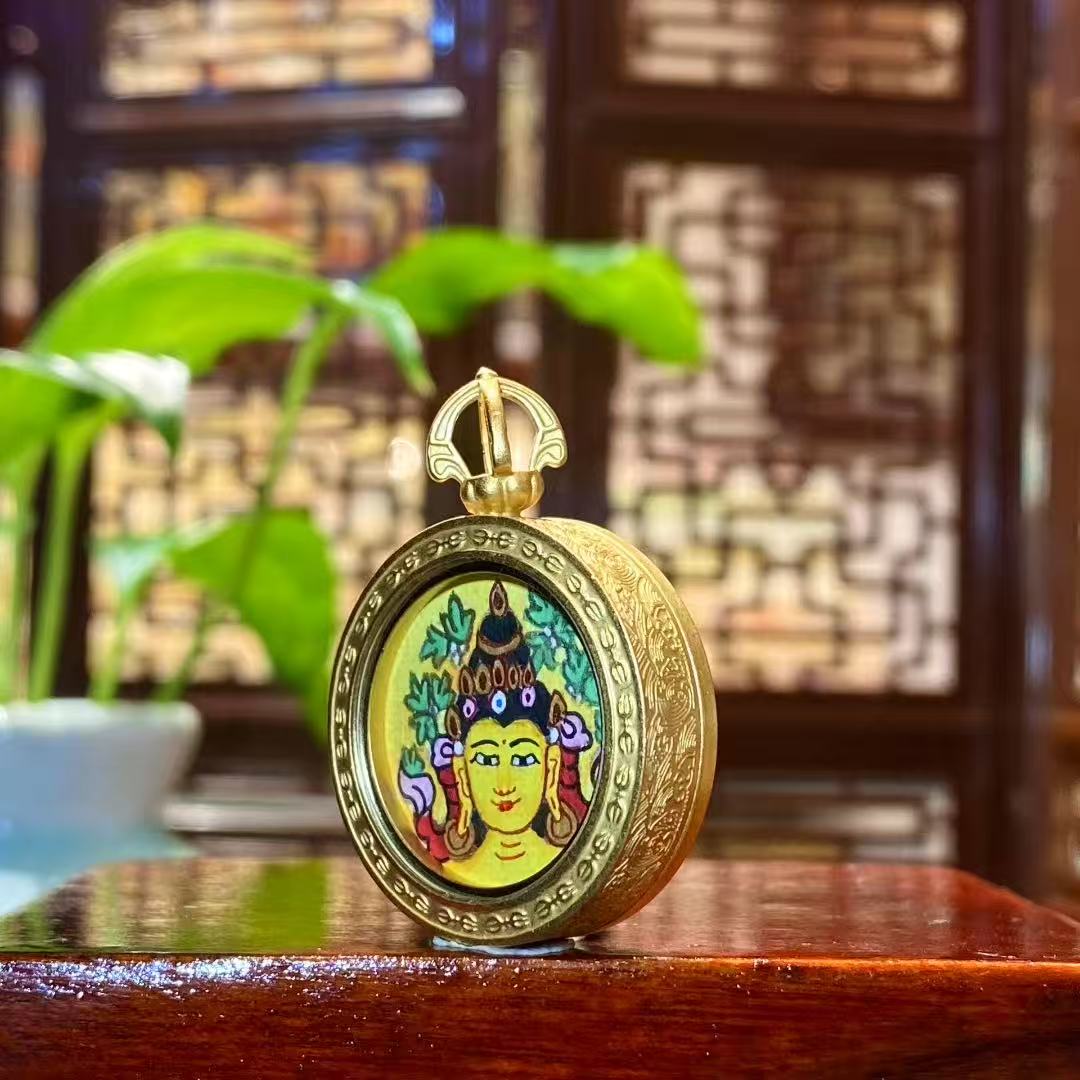 Side view of a hand-painted Manjushri Bodhisattva mini thangka pendant showing the circular titanium steel Gau box frame