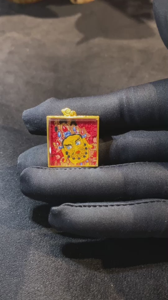 Close-up view of a double-sided hand-painted Yellow Jambhala and treasure-spitting mongoose mini Thangka pendant in an 18K gold Gau box