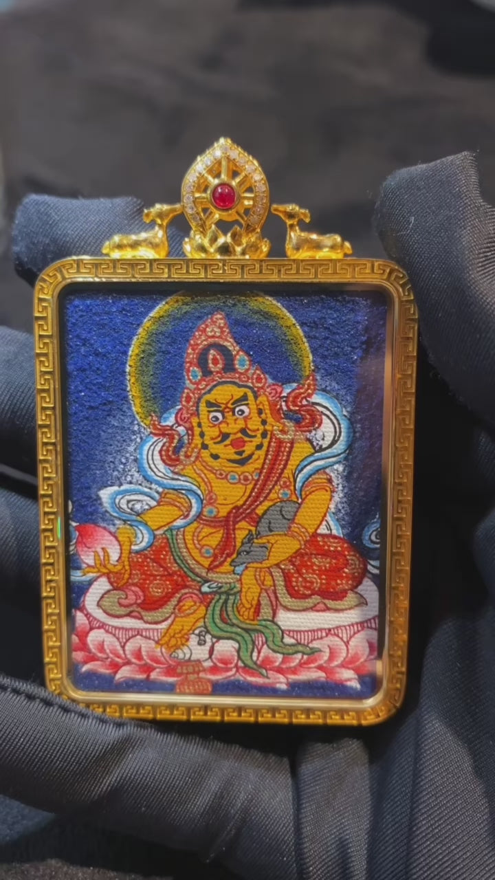 Close-up video of a double-sided Tibetan thangka pendant featuring Yellow Jambhala and Green Tara, fully hand-painted with 18K gold in the Rebgong tradition and set in an 18K gold gau box with sapphire crystal mirror