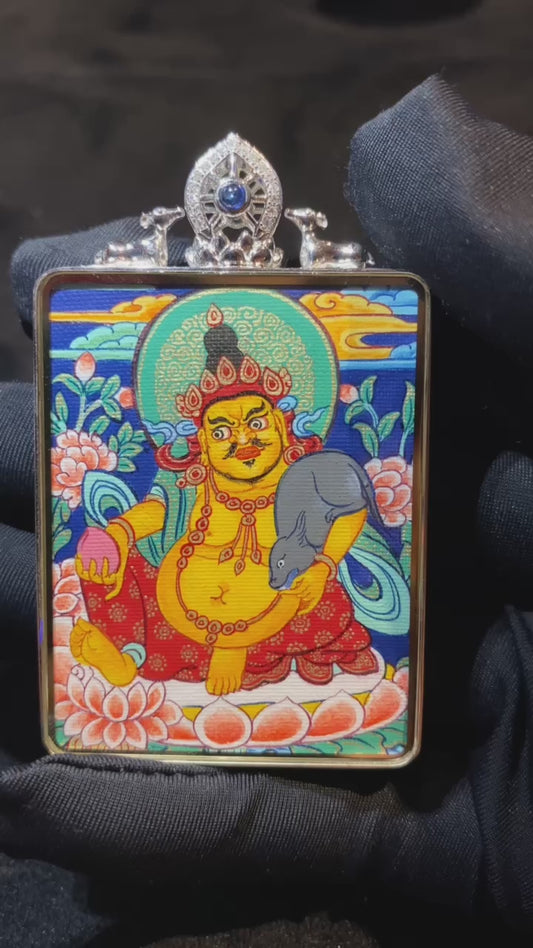 Close-up video of a compact 49×38mm double-sided Tibetan thangka pendant featuring Yellow Jambhala and Green Tara, fully hand-painted with 18K gold in the Rebgong tradition and encased in an 18K gold gau box with sapphire crystal mirror, ideal for daily wear