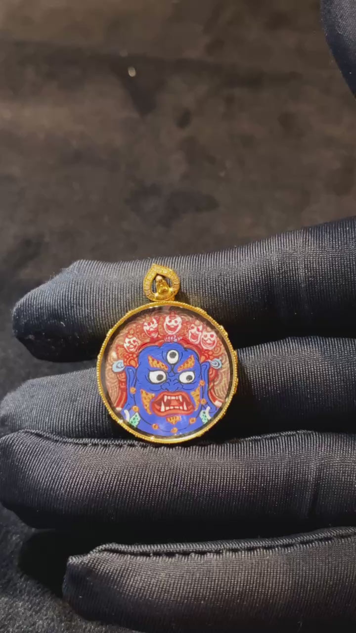 Close-up video of round Mahakala thangka pendant hand-painted in 18K gold, showing double-sided Rebgong artwork, Gau box details, sapphire crystal, and compact 21mm form