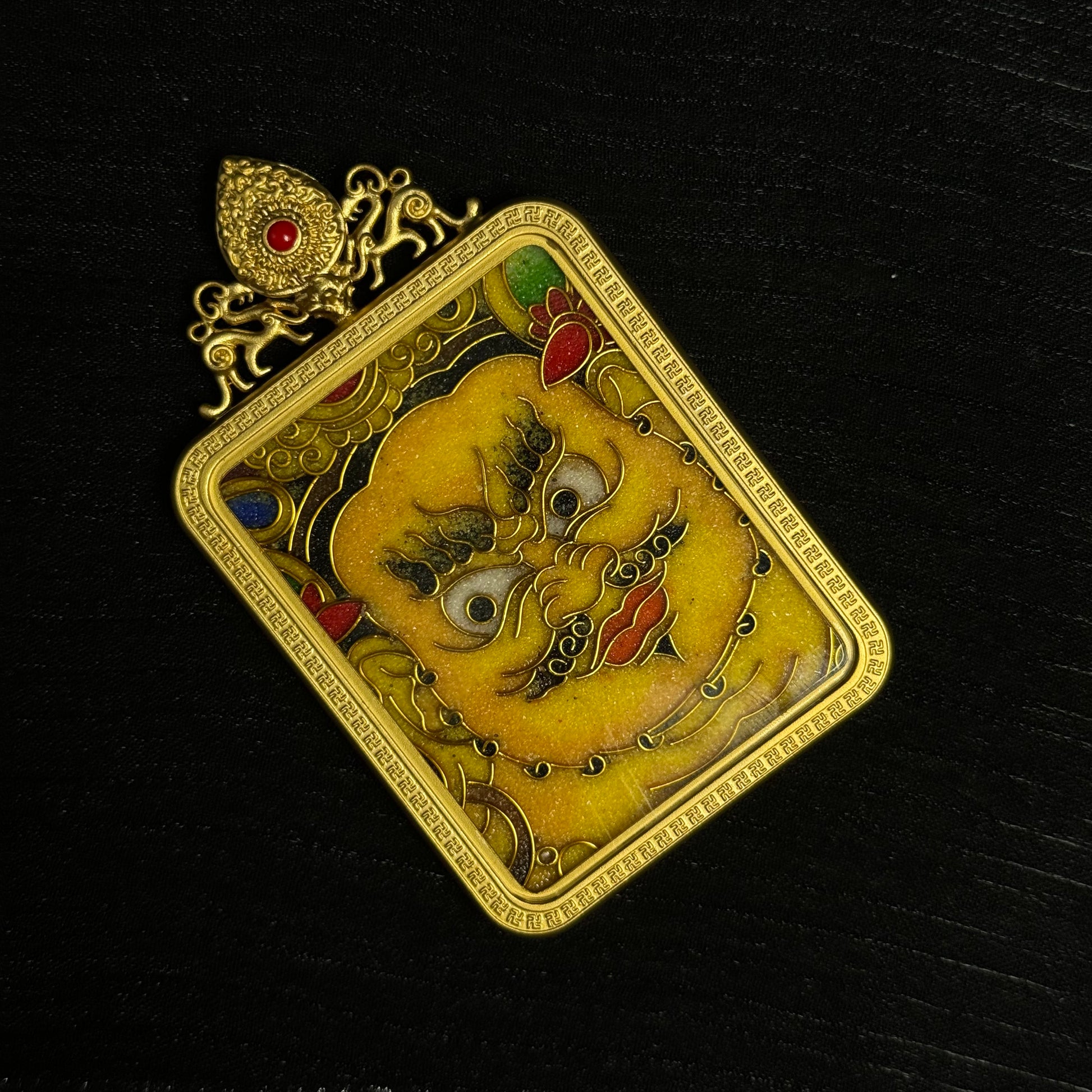 Decorative cloisonné Yellow Jambhala mini thangka pendant displayed at a tilted angle, emphasizing gold-plated copper craftsmanship and intricate Tibetan design elements.